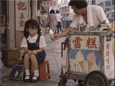Mei-ling on a low stool beside an ice cream cart as she is offered a cone
